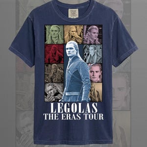 May include: Navy blue t-shirt featuring a collage of images of Legolas from The Lord of the Rings. The graphic includes multiple portraits and the text "LEGOLAS THE ERAS TOUR" in white. The shirt is made of a soft material and has a crew neck.