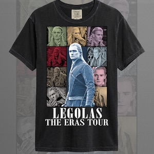 May include: Black t-shirt featuring a collage of images of Legolas from The Lord of the Rings. The design includes the text "LEGOLAS THE ERAS TOUR" in white. The shirt is made of a soft material.