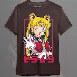 May include: A dark brown short-sleeve t-shirt featuring a graphic of the anime character Sailor Moon with blonde hair in buns, wearing a white and blue sailor-style uniform with a red bow. The text reads "MagnuM" and "美少女戦士セーラームーン".