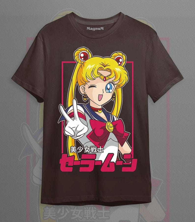 May include: A dark brown short-sleeve t-shirt featuring a graphic of the anime character Sailor Moon with blonde hair in buns, wearing a white and blue sailor-style uniform with a red bow. The text reads "MagnuM" and "美少女戦士セーラームーン".