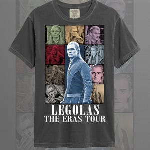 May include: Graphite-colored t-shirt featuring a collage of images of Legolas from The Lord of the Rings. The shirt includes the text "LEGOLAS THE ERAS TOUR" in white font. The shirt is made of a soft material.