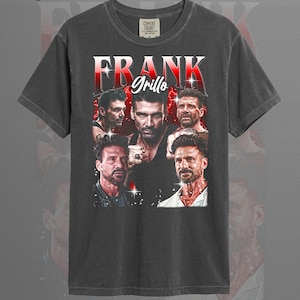 May include: Graphite-colored t-shirt featuring a collage of images of Frank Grillo, with the name "FRANK Grillo" in a red and white design. The shirt is a Comfort Colors brand.