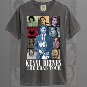 Puede incluir: Camiseta color pimienta con un collage de imágenes de Keanu Reeves. El gráfico incluye el texto "KEANU REEVES THE ERAS TOUR" en blanco. La camiseta es de la marca Comfort Colors.