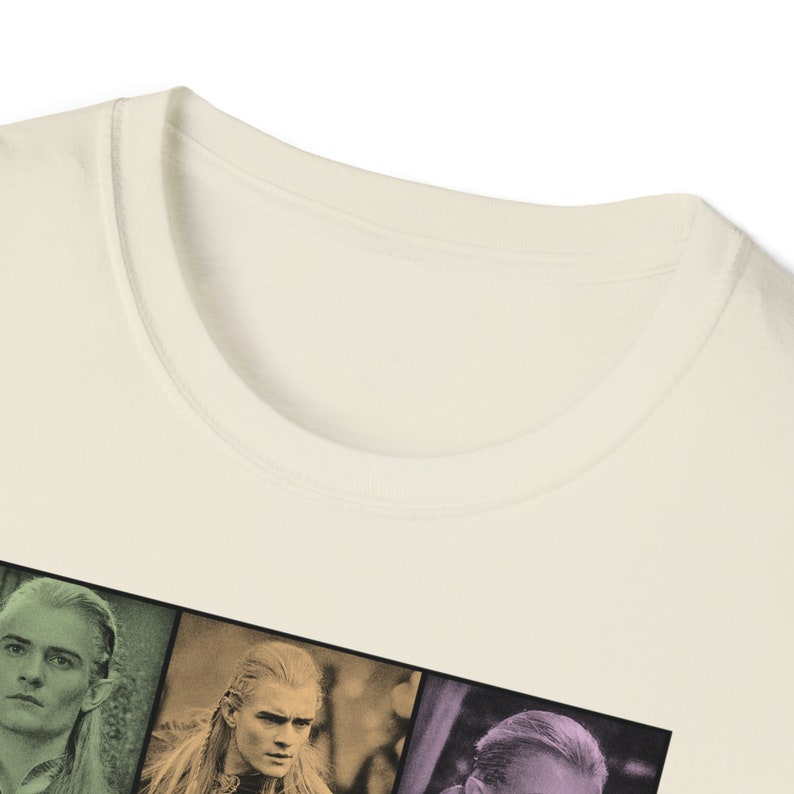 May include: Cream-colored t-shirt featuring a graphic of three characters from a fantasy film. The graphic is divided into color-blocked sections. The shirt has a crew neck and short sleeves. The fabric appears to be a soft cotton blend.