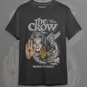 Könnte beinhalten: Schwarzes T-Shirt mit einem Grafikdesign aus dem Film "The Crow". Das Design zeigt den Filmtitel, ein Porträt der Figur und den Satz "Believe in Angels". Das Shirt hat auch den Text "It can't rain all the time..." und die Marke "Magnum".