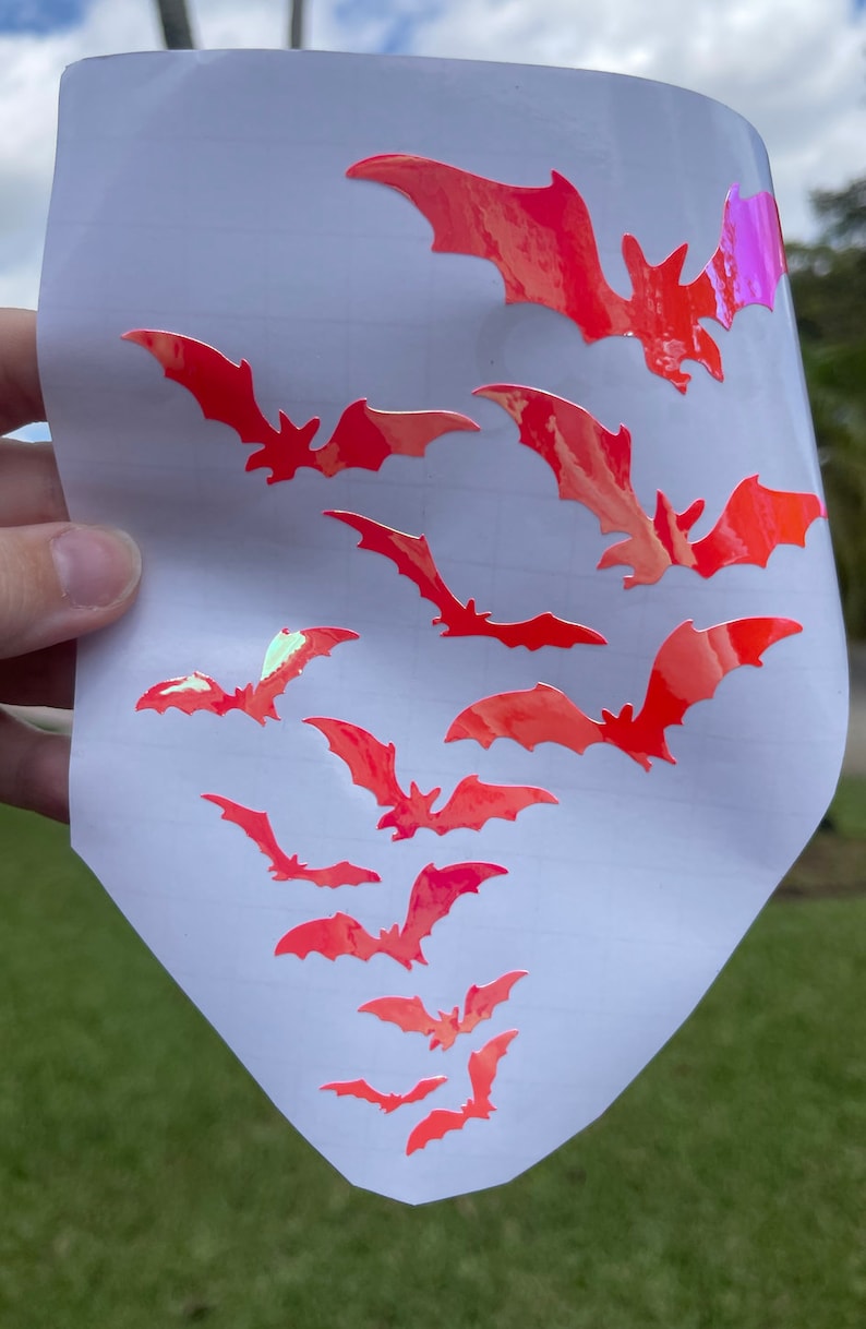 May include: A sheet of white paper with multiple pink iridescent bat stickers. The bats are various sizes and are arranged in a random pattern.