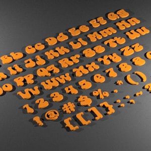 May include: Orange felt letters and numbers in a retro style font. The letters are arranged in alphabetical order and the numbers are in numerical order. There are also punctuation marks and symbols.