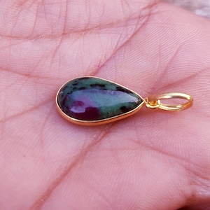May include: A teardrop-shaped pendant with a gold-colored setting. The gemstone features a mix of deep red and green hues. The pendant is designed for use as a necklace.