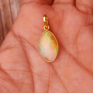 Op de afbeelding: Een gouden hanger met een peervormige, iriserende opaalsteen. De opaal toont een mix van kleuren, waaronder geel, oranje en groen. De hanger heeft een eenvoudig, elegant ontwerp, geschikt voor dagelijks gebruik of speciale gelegenheden.