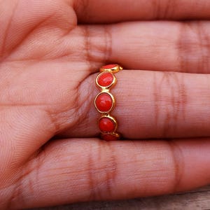 May include: A gold ring with five round, bright red stones. The ring is set in a gold band and is shown on a person's finger. The ring is a piece of jewelry.