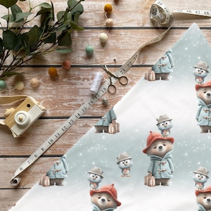 Może przedstawiać: Jasnoniebieska i biała tkanina we wzory z ilustracjami niedźwiedzi i pingwinów w płaszczach i kapeluszach, niosących walizki. Tkanina jest ozdobiona płatkami śniegu. Widoczna jest również miarka, nożyczki i nić.