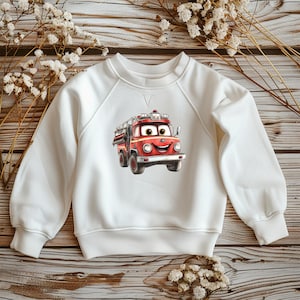 Könnte beinhalten: Weißes Sweatshirt mit einem Cartoon-Feuerwehrwagen-Design. Der Feuerwehrwagen ist rot mit schwarzen und silbernen Details, einem lächelnden Gesicht und einer Leiter. Das Sweatshirt hat einen Rundhalsausschnitt und lange Ärmel.