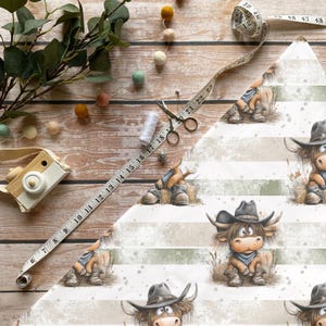 Könnte beinhalten: Stoff mit einem sich wiederholenden Muster einer Cartoon-Hochlandkuh mit Cowboyhut und Stiefeln. Der Hintergrund hat weiße und grüne Streifen. Ein Maßband, eine Schere, Faden und eine Spielzeugkamera liegen auf einer Holzoberfläche.