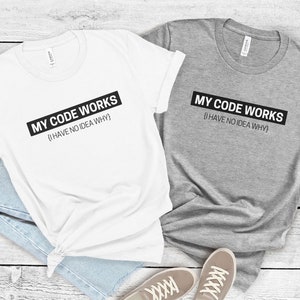 May include: Two t-shirts with the text "MY CODE WORKS {I HAVE NO IDEA WHY}" printed on them. One t-shirt is white and the other is gray.