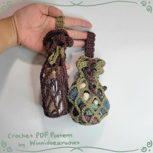 Puede incluir: Dos bolsas de crochet con cordones de ajuste. Una bolsa es marrón y verde y contiene una botella de vidrio. La otra bolsa es marrón, verde y azul y contiene pequeñas bolas de crochet. Las bolsas están etiquetadas "Crochet PDF Pattern by Winniidoescrotchet".