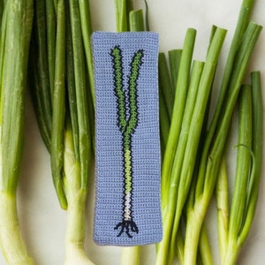 K&ouml;nnte beinhalten: Ein geh&auml;keltes gr&uuml;nes Zwiebel-Lesezeichen mit blauem Hintergrund. Das Lesezeichen ist von echten gr&uuml;nen Zwiebeln umgeben.