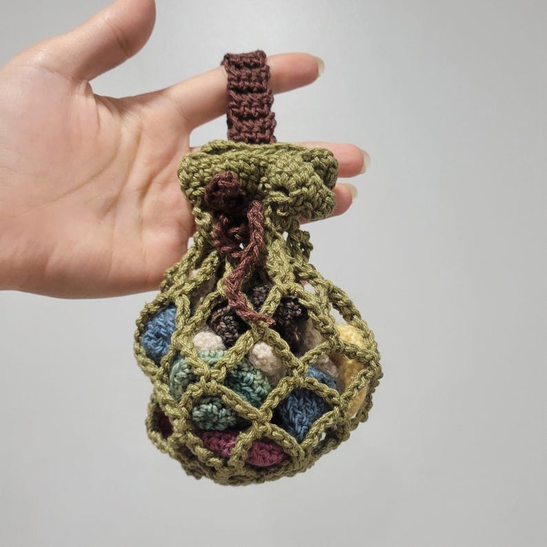 Pu&ograve; includere: Una piccola borsa all'uncinetto con un cordoncino di chiusura marrone e un manico marrone. La borsa &egrave; piena di palline colorate all'uncinetto.