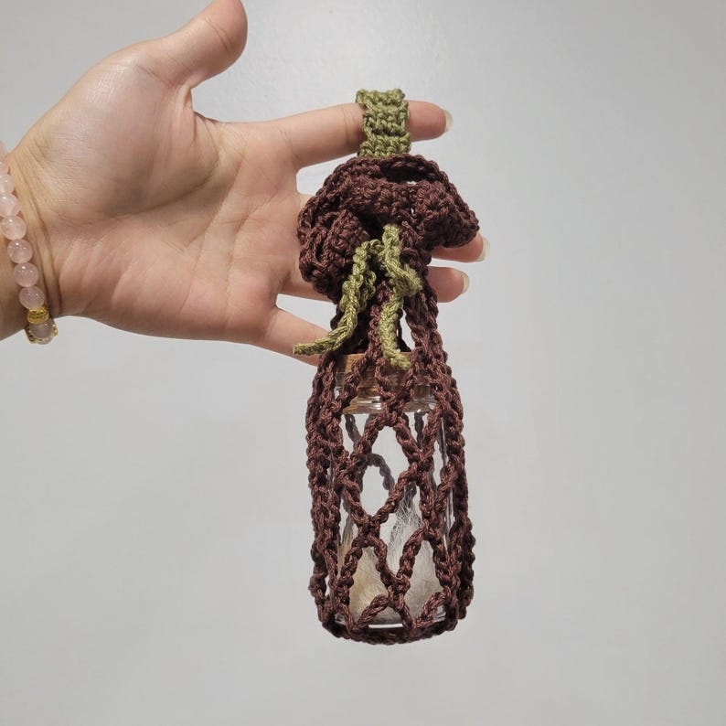 Pu&ograve; includere: Un porta bottiglie in crochet marrone con una parte superiore in crochet verde. Il porta bottiglie ha una chiusura a cordoncino ed &egrave; perfetto per riporre piccoli oggetti.