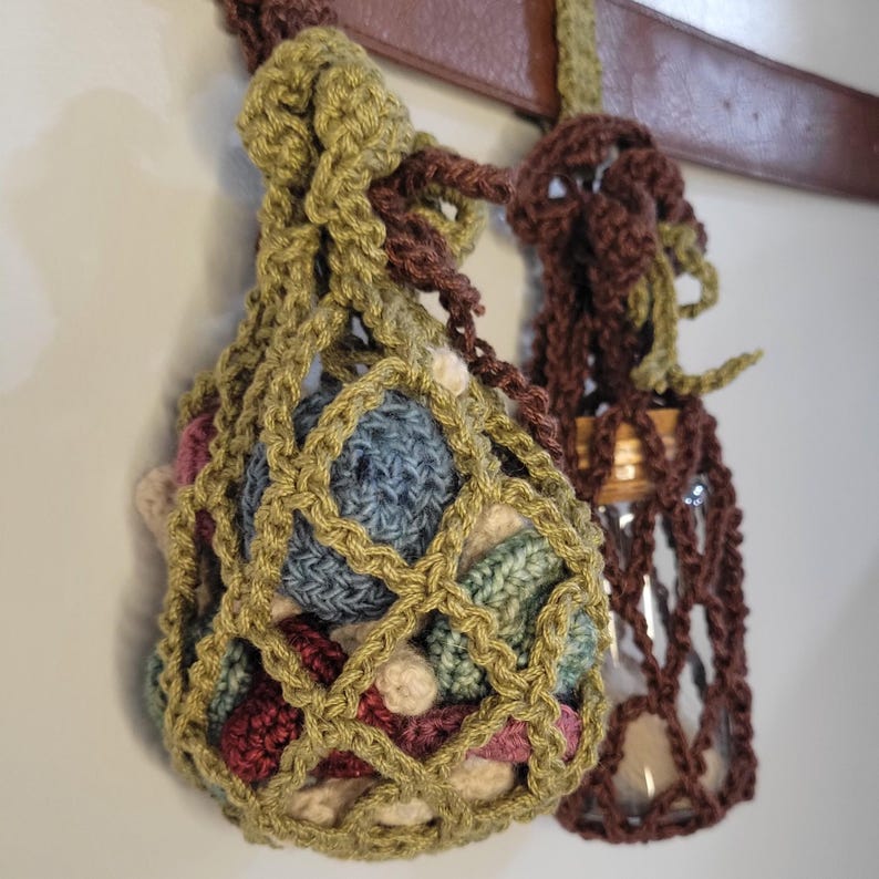 Pu&ograve; includere: Una borsa a uncinetto con chiusura a cordoncino, piena di palline colorate all'uncinetto. La borsa &egrave; appesa a una cinghia di cuoio marrone.