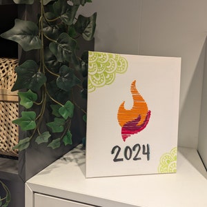 May include: A white canvas with a green and yellow mandala design in the top right corner. A red and orange flame design is in the center of the canvas with the year 2024 written in black below it.
