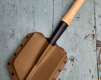 May include: A brown leather sheath with black rivets and a wooden handle attached to a black metal shovel head.