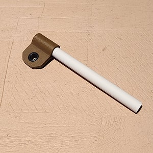 May include: A brown plastic part with a white tube extending from it. The brown piece has a circular hole with a black grommet. The white tube is cylindrical and appears to be made of plastic.