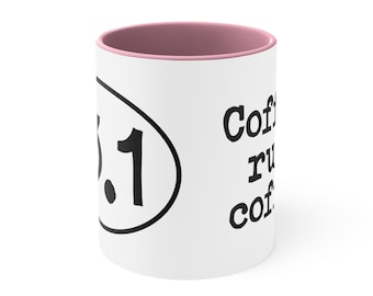 May include: White ceramic coffee mug with a pink rim. The mug has a black oval with the number "3.1" inside and the text "Coffee runs on coffee" on the right side.
