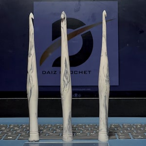 May include: Three crochet hooks with black and white marbled handles. The hooks are 4.0 mm, 4.5 mm, and 5.0 mm. The hooks are on a laptop keyboard.