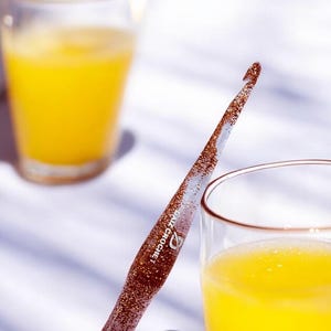 May include: A clear, ergonomic crochet hook filled with copper-colored glitter particles. The tool features a tapered shaft with a hook at the top and the white text "DAIZ CROCHET" printed along the center of the handle, showcasing a smooth finish.
