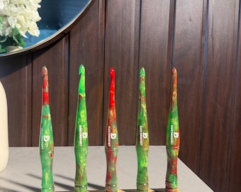 May include: Five crochet hooks with marbled red and green resin handles, each featuring the white text "DAIZ CROCHET" and a logo. The hooks are displayed upright in a rectangular wooden stand with the text "DAIZ CROCHET" engraved on the front.