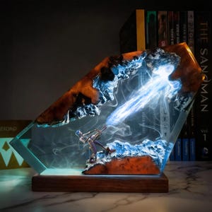 Könnte beinhalten: Ein einzigartiges Kunstwerk aus Harz, das eine Figur mit einer Waffe zeigt, die einen blauen Energiestrahl aussendet. Das Kunstwerk ist in einem klaren, abgewinkelten Harzblock mit braunen und blauen Akzenten eingeschlossen, der auf einem Holzsockel steht.