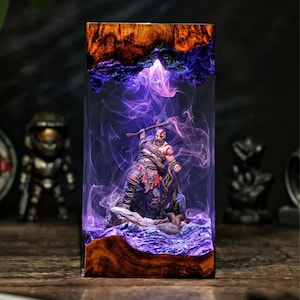 May include: A rectangular resin art piece featuring a detailed figure of a warrior with an axe, set against a backdrop of swirling purple and white smoke. The base and top are made of wood, with a dark background.
