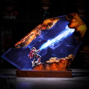 May include: A rectangular resin and wood lamp featuring a miniature figure in a red cape firing a bright blue energy beam. The piece is set on a dark wooden base, with natural wood edges framing the translucent blue resin center.