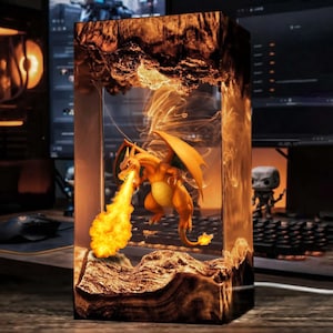 May include: A rectangular resin art piece featuring a fiery orange Charizard figure spewing flames. The artwork has a layered, textured appearance with warm orange and brown tones, creating a dynamic, fantasy-themed display.