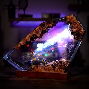 May include: A unique resin sculpture featuring a superhero figure in a dynamic pose, emitting a bright energy beam. The sculpture is encased in a clear resin with a wooden frame, mounted on a wooden base. The artwork showcases a blend of action and artistic craftsmanship.