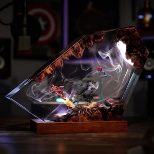 May include: A resin art piece with miniature superhero figures. The clear resin displays Iron Man, Spider-Man, and the Hulk, with white and purple smoke effects. The base is a dark wooden rectangle. The piece is a unique decorative item.