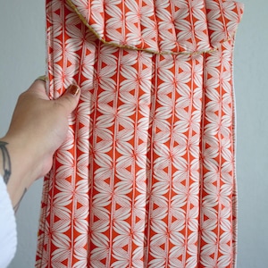 May include: Quilted fabric sleeve in a vibrant orange and white floral pattern. The sleeve has a flap closure and a yellow trim. The design is a repeating pattern of white leaf-like shapes on an orange background.