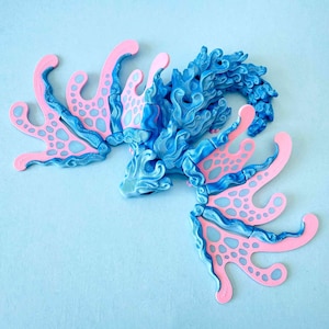 May include: A blue and pink dragon sculpture with intricate details. The dragon features a blue body with pink accents on its wings and tail. The sculpture is set against a light blue background. The image also includes the text "TINY makery" and "DIGITAL FILE".