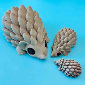 May include: Three brown ceramic hedgehogs of varying sizes. The largest hedgehog is facing the viewer with its eyes open. The two smaller hedgehogs are facing the side.