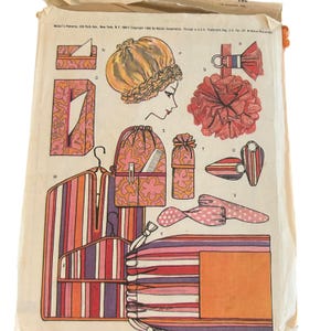 May include: A vintage McCall's sewing pattern envelope featuring illustrations of various fabric accessories including a shower cap, tissue box covers, a drawstring bag, a garment bag, and decorative items in pink, orange, and purple floral and striped prints.