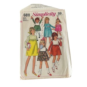 Può includere: Una busta per cartamodello vintage Simplicity 6811 per un abito da bambino taglia 6 con una misura del torace di 24 pollici. Il fronte presenta illustrazioni di sei bambini che indossano vari stili di abiti in giallo, verde, blu, rosa e rosso.