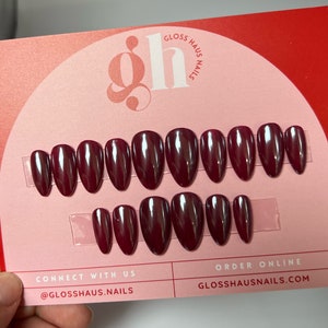May include: A set of 10 burgundy press-on nails with a glossy finish. The nails are arranged in two rows on a pink and red background with the text "Gloss Haus Nails" and "@glosshaus.nails".