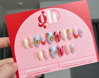 May include: A set of press-on nails on a pink card with the text "Gloss Haus Nails." The nails feature various designs, including oranges, lobsters, lemons, and starfish. The card is red and pink with the Etsy shop URL.