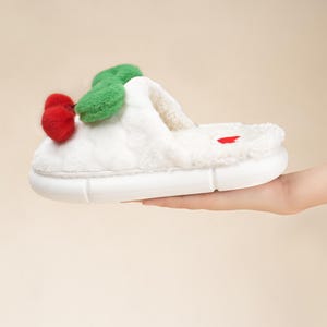 Pu&ograve; includere: Pantofola in peluche bianca con design a ciliegia. La pantofola presenta una ciliegia rossa con foglie verdi sulla parte superiore e un cuore rosso sul plantare. La suola &egrave; bianca e ha un design strutturato.