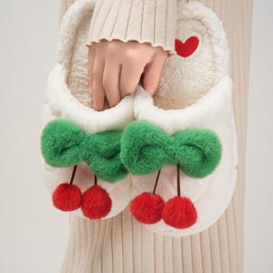 Pu&ograve; includere: Morbide pantofole bianche con fiocchi verdi e ciliegie a pompon rosse. Un piccolo cuore rosso &egrave; cucito sul lato. Queste morbide pantofole sono progettate per l'uso in casa.