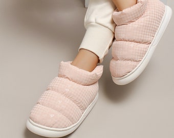 Può includere: Un paio di pantofole da interno imbottite rosa con suole bianche. Le pantofole hanno un design trapuntato e gonfio e sono realizzate in un materiale morbido e confortevole.