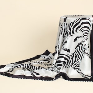 May include: A white silk scarf with a black and white zebra print. The scarf has a black border with white dots.