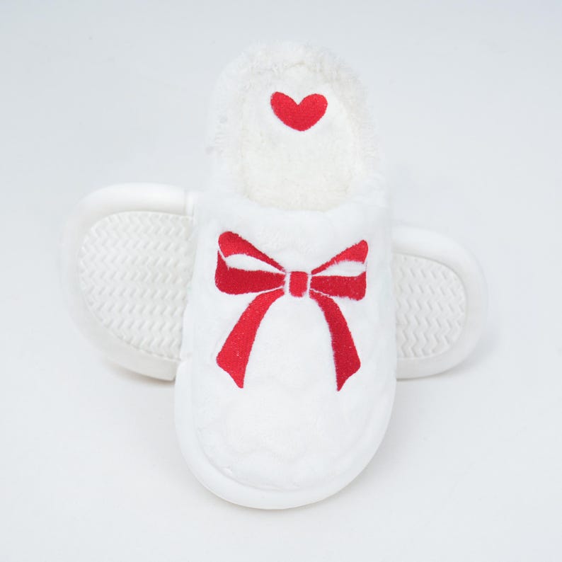 Pu&ograve; includere: Pantofola in peluche bianca con un design a fiocco e cuore rosso. La pantofola ha un interno morbido e strutturato e una suola antiscivolo. Il fiocco &egrave; ricamato sul davanti e un piccolo cuore &egrave; ricamato in alto.