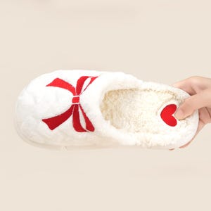 Pu&ograve; includere: Pantofola bianca con un design a fiocco rosso e un accento a cuore rosso. La pantofola ha un esterno morbido e felpato e un interno soffice. La pantofola &egrave; progettata per l'uso in casa e offre comfort e calore.