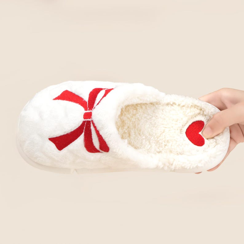 Pu&ograve; includere: Pantofola bianca con un design a fiocco rosso e un accento a cuore rosso. La pantofola ha un esterno morbido e felpato e un interno soffice. La pantofola &egrave; progettata per l'uso in casa e offre comfort e calore.